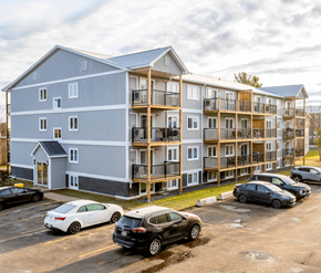 Fredericton apartment for rent - A large building with a parking lot in front of it.