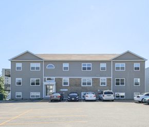 Saint John apartment for rent - A grey building with a parking lot in front of it.