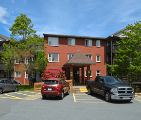 Halifax apartment for rent - A red car is parked in a parking lot in front of a brick building.