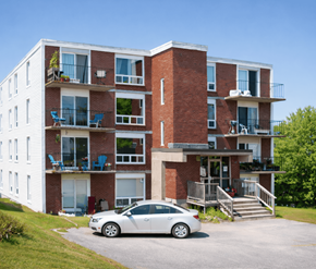 Saint John apartment for rent - A white car is parked in front of a red brick apartment building.