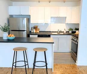 Ottawa apartment for rent - A kitchen with white cabinets and a black countertop with a refrigerator, stove, and two bar stools.
