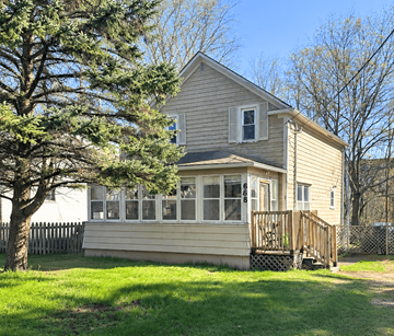 Fredericton apartment for rent - A house with a deck and a tree in front.