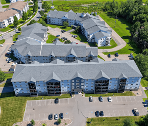 Fredericton apartment for rent - A large building with a grey roof and a parking lot in front.