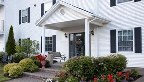 Stratford apartment for rent - A white house with a black awning and a red flower bed in front.