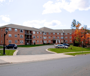 Fredericton apartment for rent - A large red brick building with a parking lot in front.