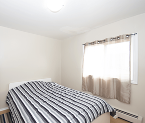 Saint John apartment for rent - A bed with a striped comforter sits in a room with a window.