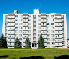 Moncton apartment for rent - A large white apartment building with balconies and trees in front.