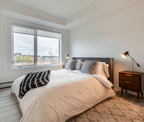 Calgary apartment for rent - A bedroom with a large bed and a window overlooking a cityscape.