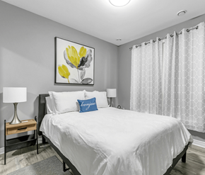 Cambridge apartment for rent - A bedroom with a large bed, a nightstand with a lamp, and a framed picture of yellow flowers on the wall.