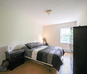 Fredericton apartment for rent - A bedroom with a bed, nightstand, and window.