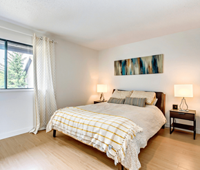 Calgary apartment for rent - A bedroom with a bed, two lamps, and a painting on the wall.