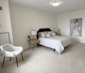 Kanata Ottawa apartment for rent - A white chair sits in a bedroom with a bed and a painting on the wall.