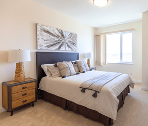 Kanata-Ottawa apartment for rent - A bedroom with a large bed, a nightstand with a lamp, and a painting on the wall.