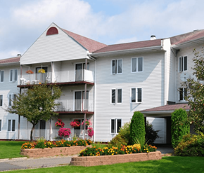 Fredericton apartment for rent - A white building with a red roof and a balcony with flowers.