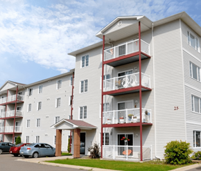 Fredericton apartment for rent - A white apartment building with red balconies and a car parked in front.