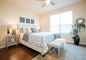 Tomball apartment for rent - A bedroom with a large bed and a bench in front of it.