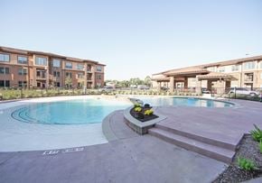 Tomball apartment for rent - A swimming pool surrounded by a building and a flower bed.