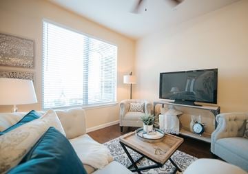 Tomball apartment for rent - A living room with a white couch, a wooden coffee table, and a television on the wall.