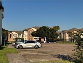 Houston apartment for rent - A silver car is parked in a parking lot in front of a building.