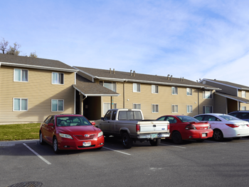 A red car is parked in a parking lot in front of a building.