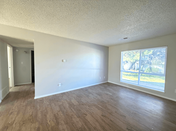 A room at mountain terrace apartments  with wooden floors and a window showing a view of a fence and trees.