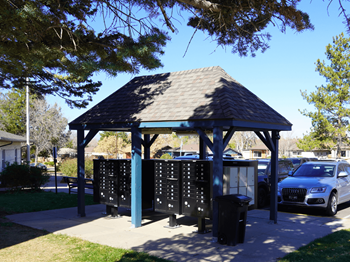 A gazebo with a roof and a signboard is surrounded by trees and a car is parked nearby.