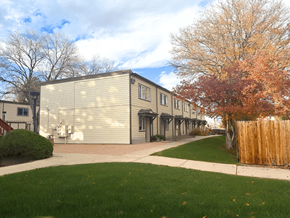 Lakewood townhouse for rent - A building with a grey facade is surrounded by a green lawn and a wooden fence.