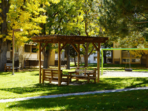 Denver apartment for rent - A wooden pergola with benches is situated in a grassy area with trees at Garden Court Apartments, Denver, CO