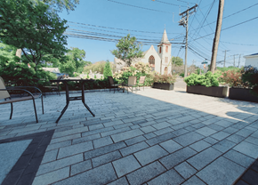 Stamford apartment for rent - A church with a steeple is in the background of a brick patio with chairs and tables.