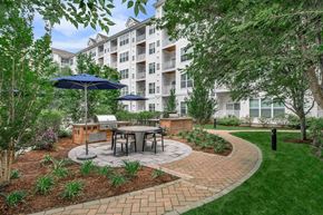 Norwalk apartment for rent - A patio with a table and chairs is surrounded by a brick border and a grassy area.