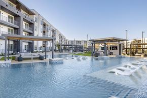 Del Valle apartment for rent - A modern pool area with a water slide and apartment buildings in the background.