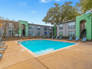 Dallas apartment for rent - A swimming pool surrounded by chairs and trees in front of a building.