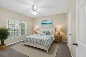 Gulf Shores apartment for rent - A bedroom with a bed, a ceiling fan, and a painting of a beach scene on the wall.