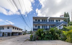 Honolulu apartment for rent - A white building with a blue roof is surrounded by greenery and power lines.