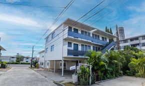 Honolulu apartment for rent - A white residential building with blue balconies is surrounded by greenery and other buildings.