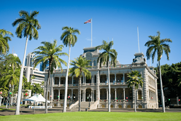 Honolulu apartment for rent - a large white building with palm trees in front of it and a flag on top