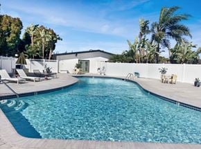 Buena Park apartment for rent - A large swimming pool surrounded by a white fence and palm trees.