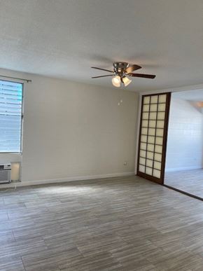 Honolulu apartment for rent - A room with a ceiling fan and light fixture, a window with blinds, and a wooden floor.