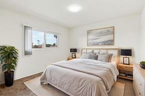 Inglewood apartment for rent - A bedroom with a large bed, a potted plant, and a painting on the wall.