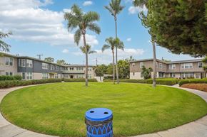 Inglewood apartment for rent - A blue trash can sits in the middle of a grassy circle in front of apartment buildings.