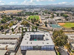 Canoga Park apartment for rent - A large white building with a green roof is in the center of a parking lot.