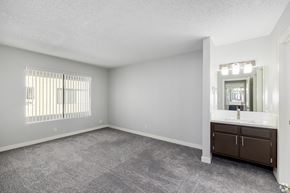 Van Nuys apartment for rent - A spacious room with a window, carpeted floor, and a bathroom with a sink and mirror.