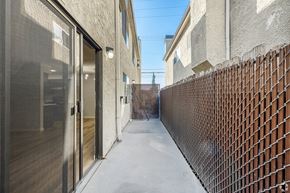 Van Nuys apartment for rent - A narrow alley with a fence on one side and a building with a glass door on the other.