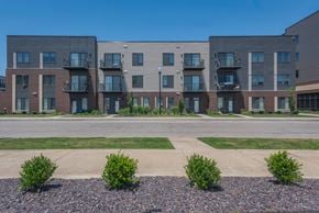 Evansville apartment for rent - Apartment complex with grey and brown buildings and green bushes in front.
