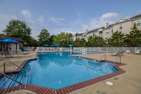 Bear triplex for rent - A large outdoor swimming pool with a red brick border and a blue umbrella.