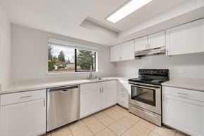 Burien apartment for rent - A kitchen with white cabinets and appliances, a stainless steel dishwasher, and a stove top oven.