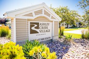 Vernal apartment for rent - A sign for Ashley Creek Village Apartments is displayed in front of a landscaped area.