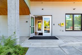 Bothell apartment for rent - A modern building entrance with a glass door and a black mat on the concrete floor.