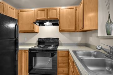 Tukwilla apartment for rent - A black refrigerator sits next to a black stove in a kitchen with wooden cabinets.