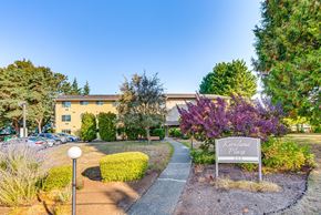 Kirkland apartment for rent - The image shows a sign that reads "Kirkland Place" in front of a building with a parking lot and trees in the background.
